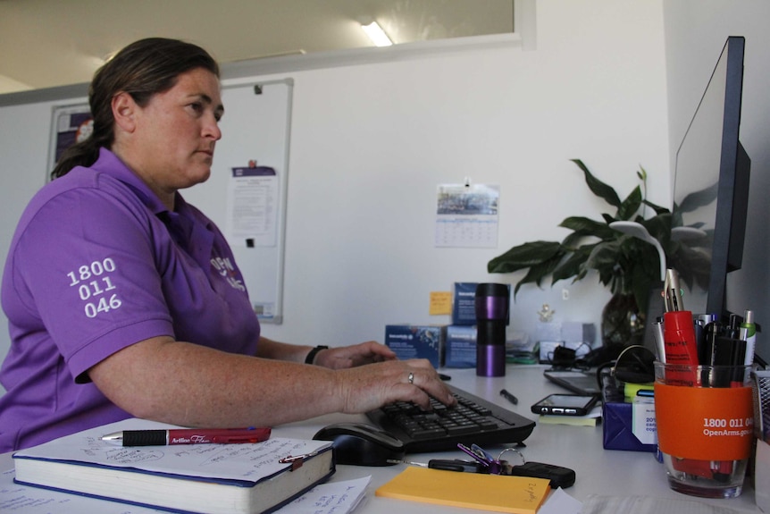 Woman in purple, logoed work shirt typing at a computer in an office.