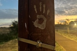 a white hand print on a brown pole at sunset