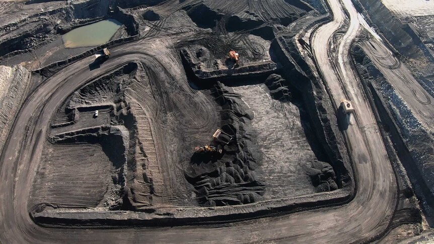 Aerial shot of an open-cut coalmine with trucks and loaders working on roadways to and from the pit