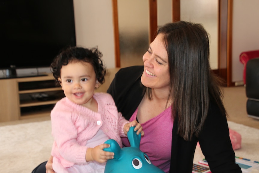 A woman is seen next to a toddler, smiling