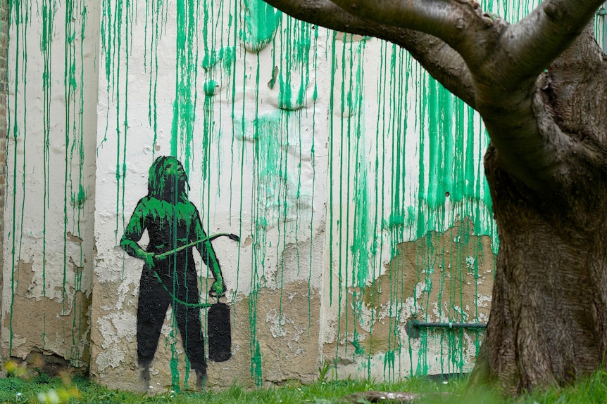 A close up of a wall with green pain and a mural of a girl holding a paint brush