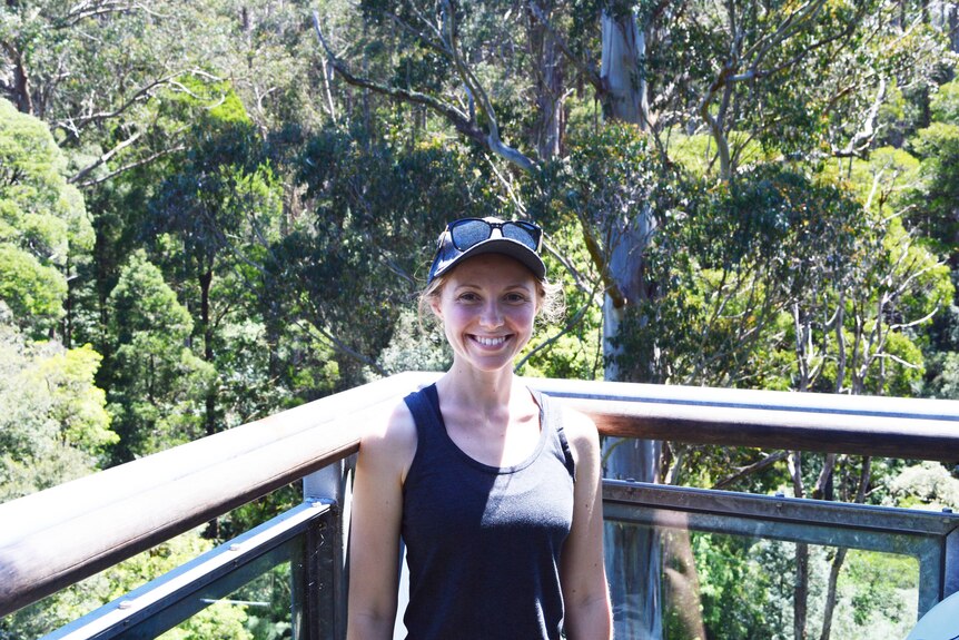 Wearing a cap, Daisy stands in the bush smiling at the camera