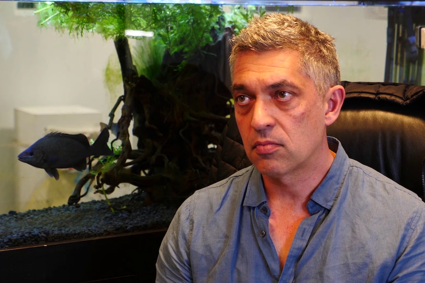 Simon Boag sitting in front of a fish tank with a native Australian fish.