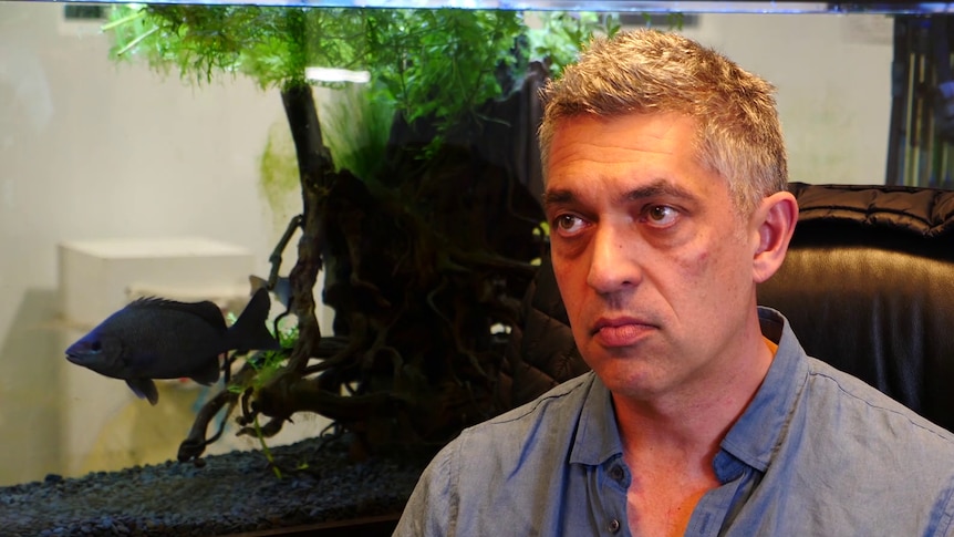 Simon Boag sitting in front of a fish tank with a native Australian fish.