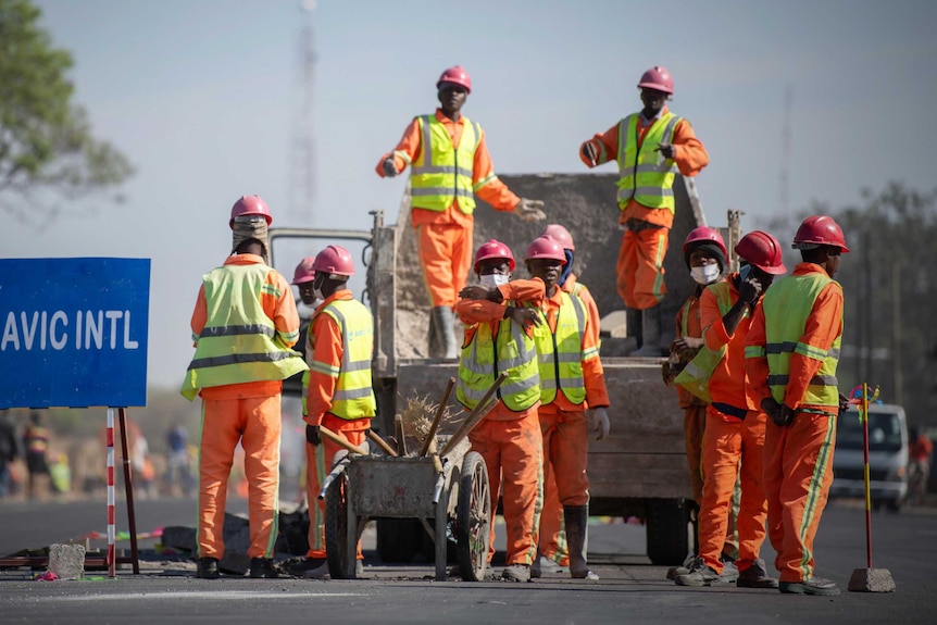 A group of men building roads in Zambia stand around a truck