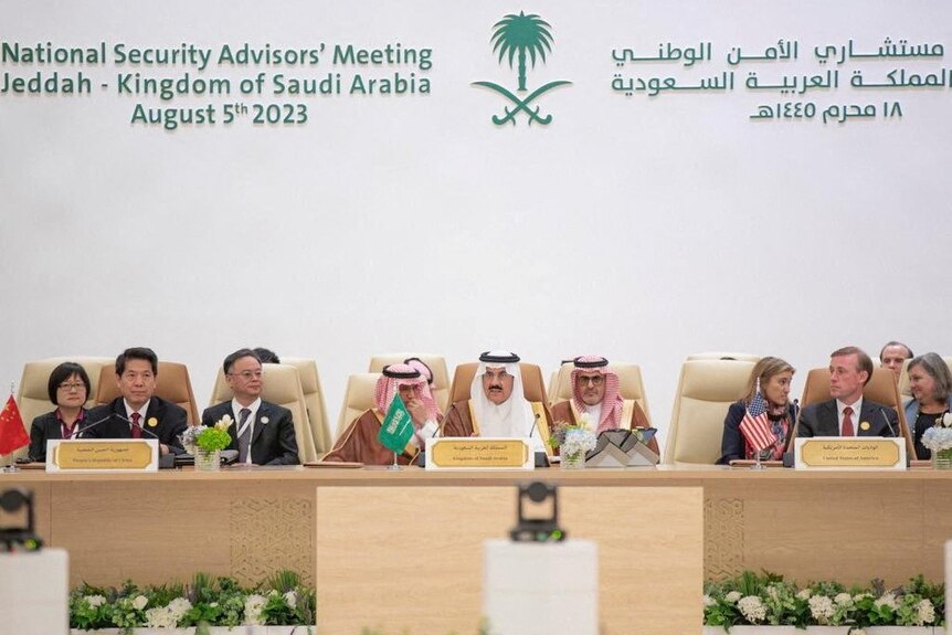 Representatives from China, the US., and Saudi Arabia sit at a long desk for official talks.