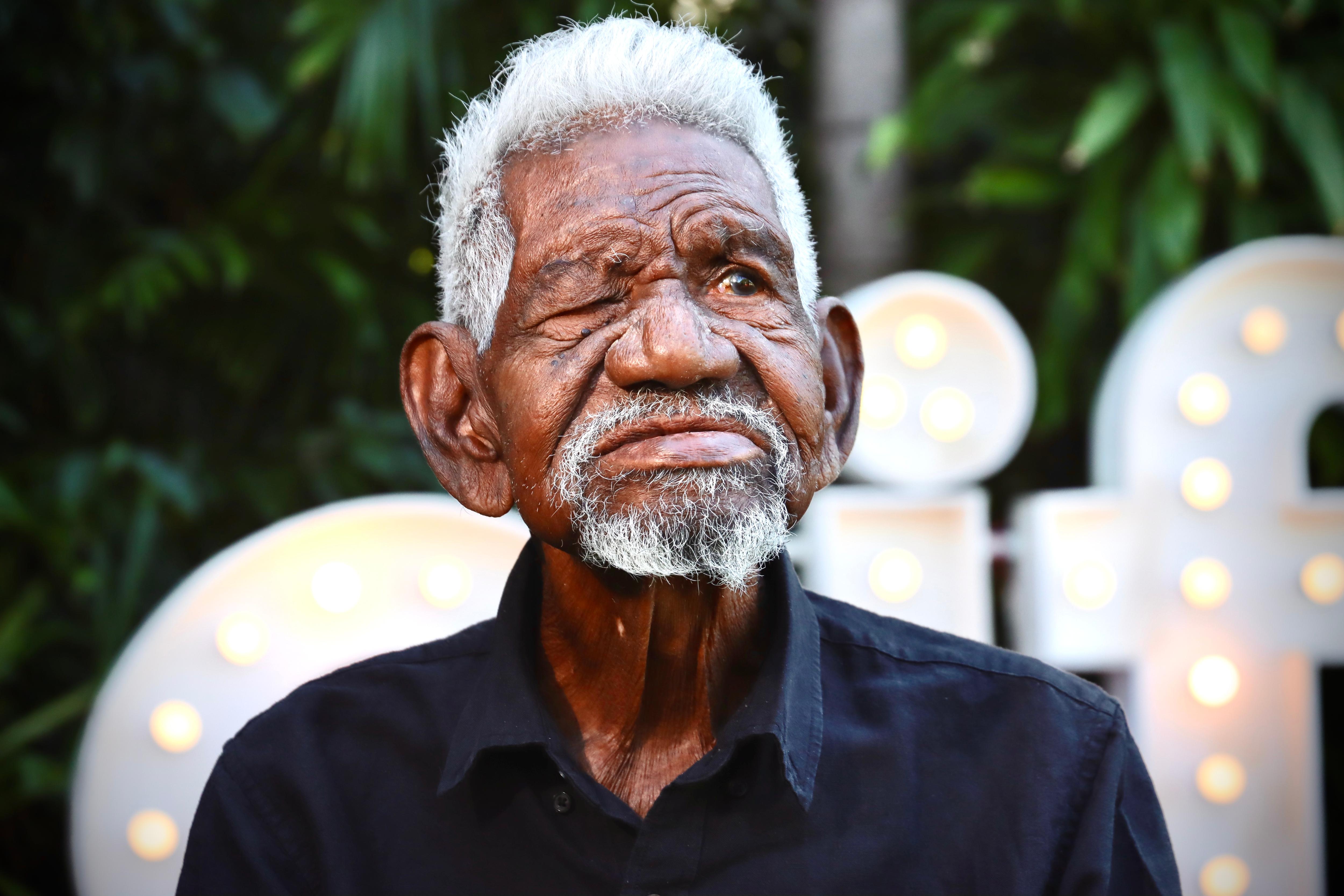 Indigenous man with grey hair and one eye looks into the distance