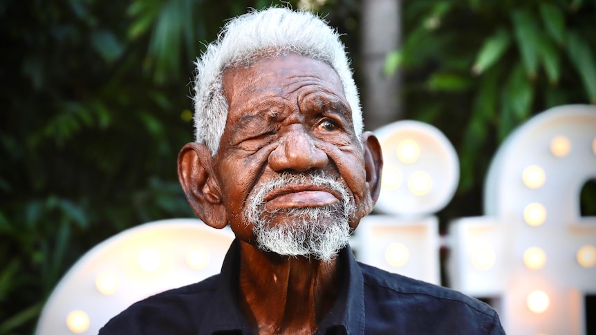Indigenous man with grey hair and one eye looks into the distance