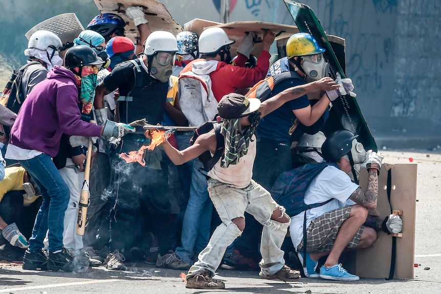 Opposition demonstrators equipped with protective hardhats, gloves and gas masks take cover behind homemade shields.