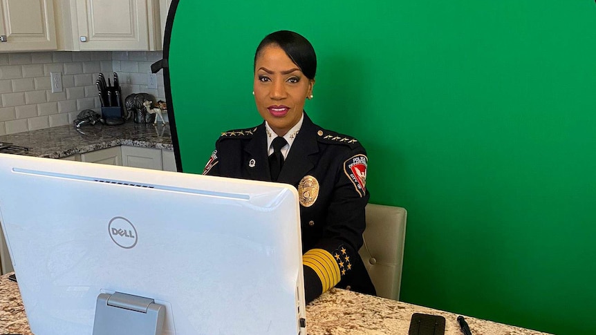 African American police chief C.J. Davies sitting at a desk in uniform in front of a green screen.