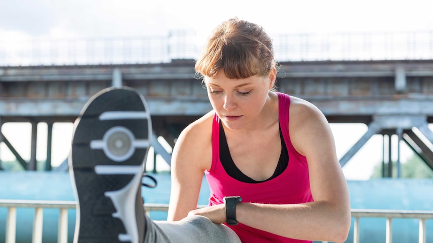 A woman doing a stretch, looking at her fitness tracker.