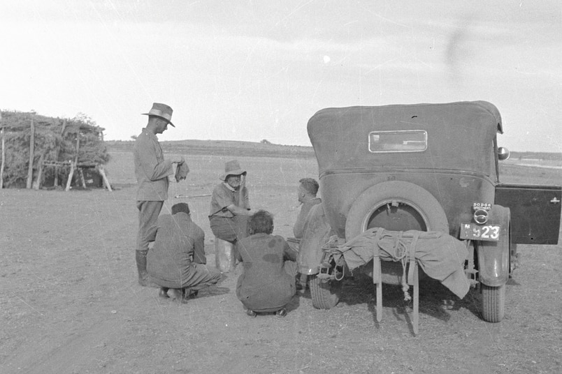 Black and white photo of men standing and sitting near a cart in the outback.