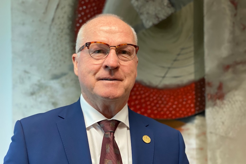 A bald, bespectacled man in a dark suit.