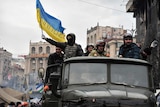 Anti-government protesters, one holding the Ukrainian national flag, drive a military vehicle through Kiev
