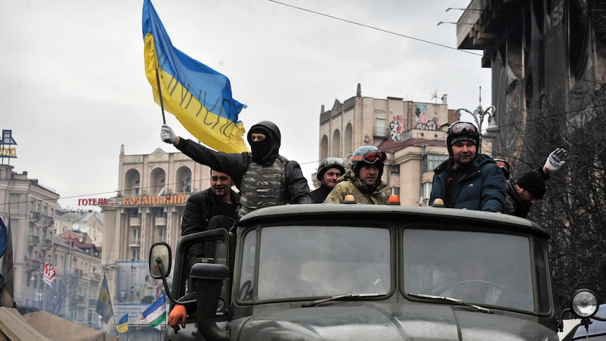 Anti-government protesters, one holding the Ukrainian national flag, drive a military vehicle through Kiev