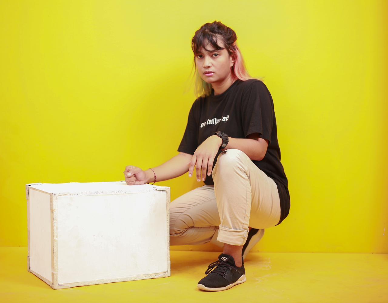 A woman in black, khaki trousers, half squatting looks at the camera.