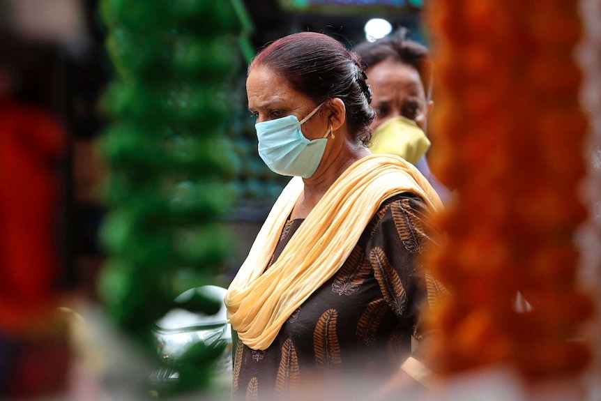 Woman with dark hair wearing mask walking through market