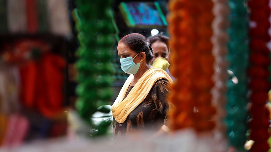 Woman with dark hair wearing mask walking through market