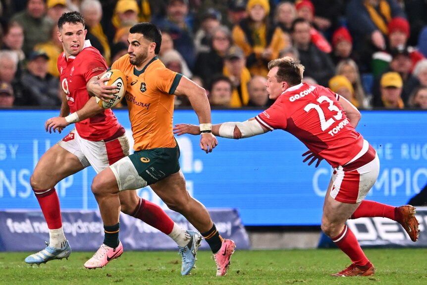 Two rugby men in red chase one rugby man in Australian colours with the ball 