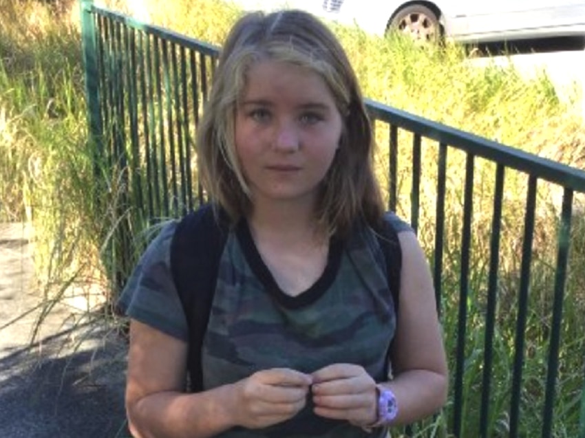 A young girl in bare feet standing near a school fence