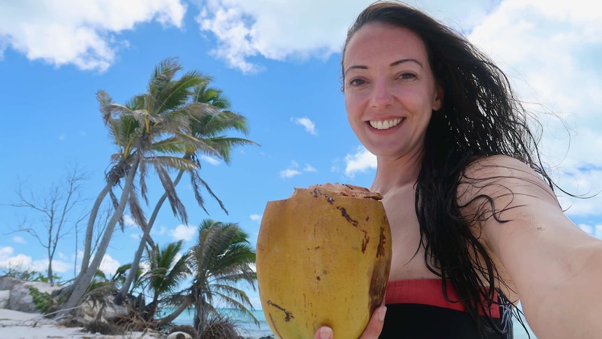 Travel writer Rachel Lees posing with a coconut and palm trees in background to depict what it's like being a travel writer.