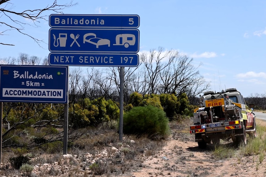 A fire truck drives past a sign saying five kilometres to Balladonia