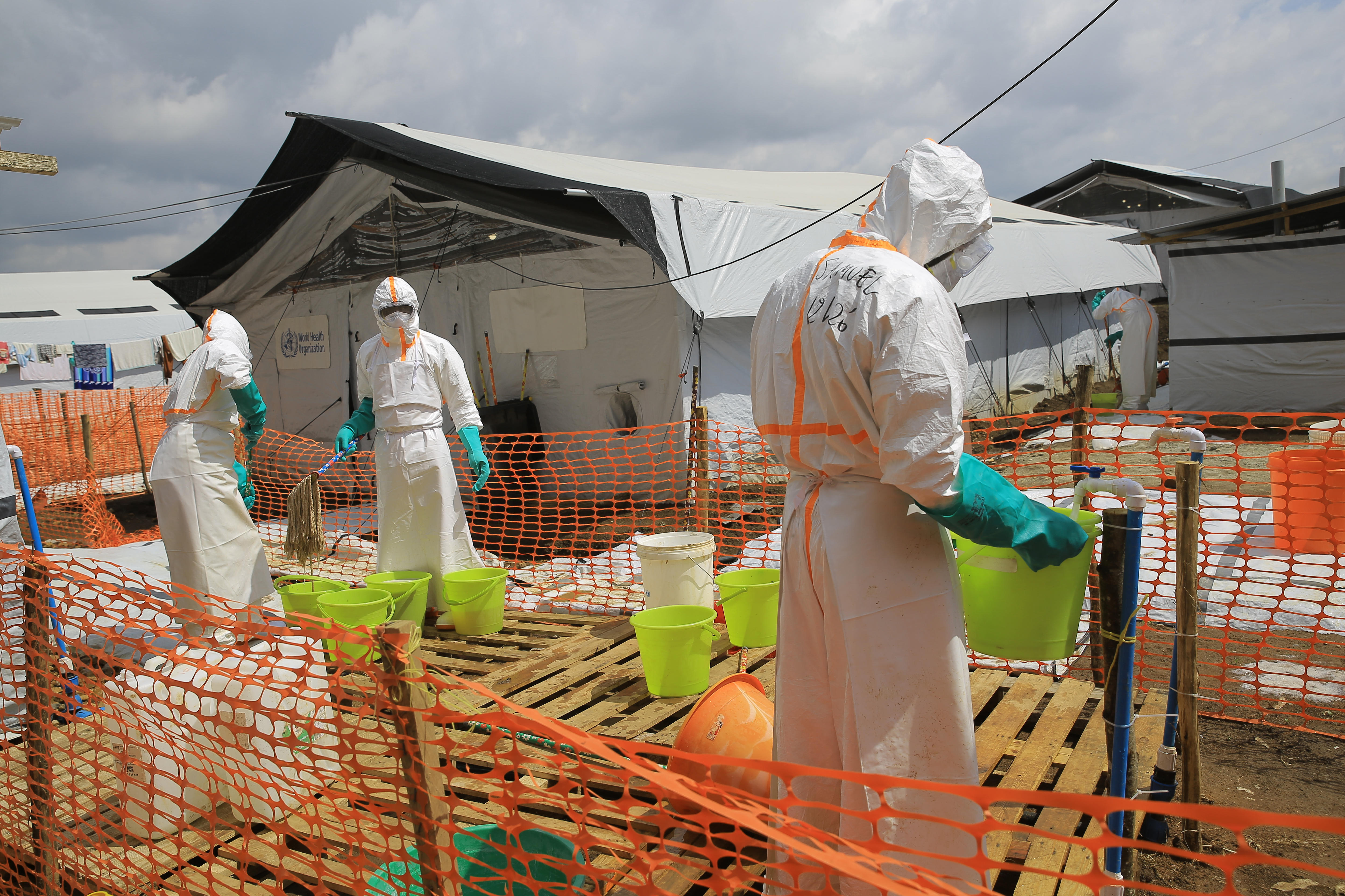 Health workers inside a fenced area in hazmat suits.
