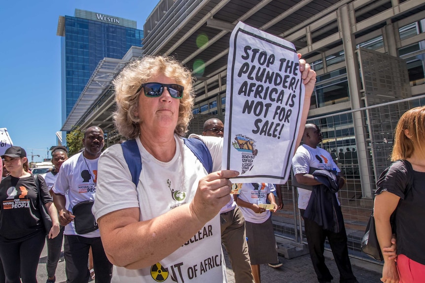 Liz McDaid at a protest holding a sign saying 'stop the plunder! Africa is not for sale.'