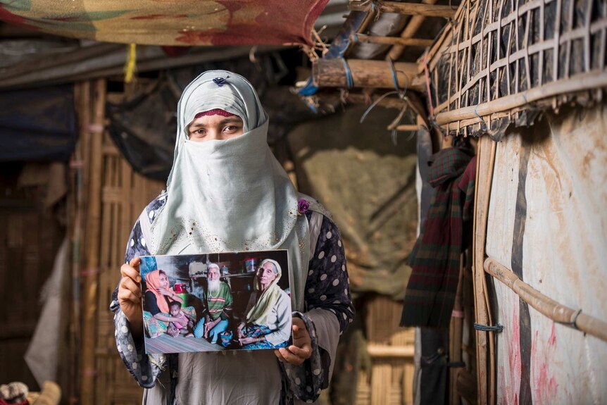 A muslim woman with her face partially covered by a veil stares at the camera while holding a photograph