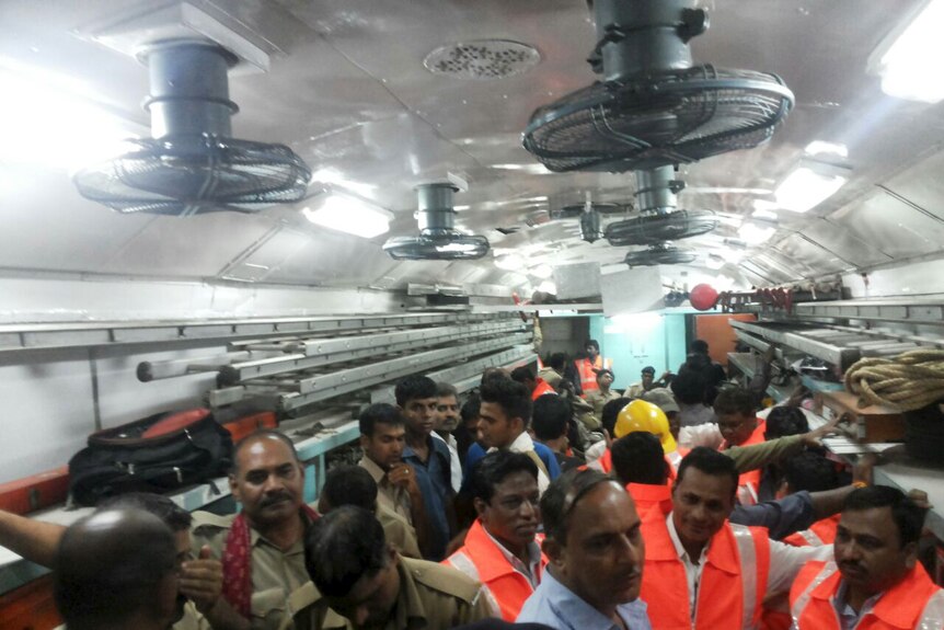 Officials and members of the rescue operation stand in a carriage of a derailed train in India