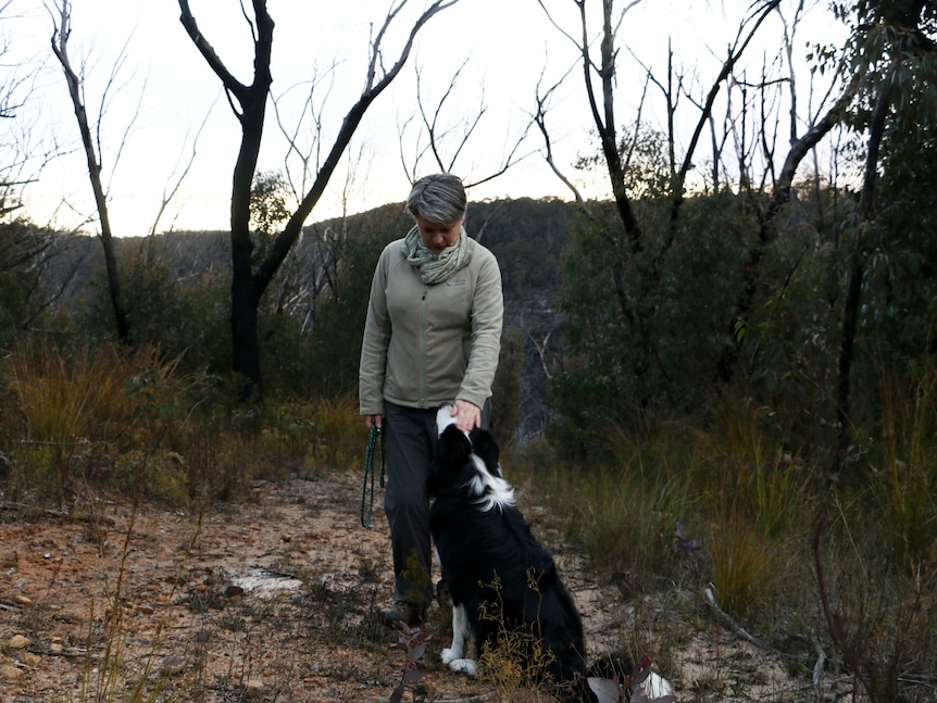 Dr Kellie Leigh stands in front of the scorched bush with her dog, Grut. 