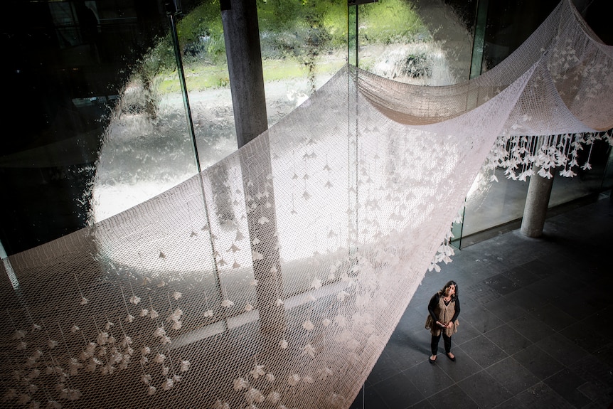 A high-angle image of a woman standing underneath a vast white woven net.