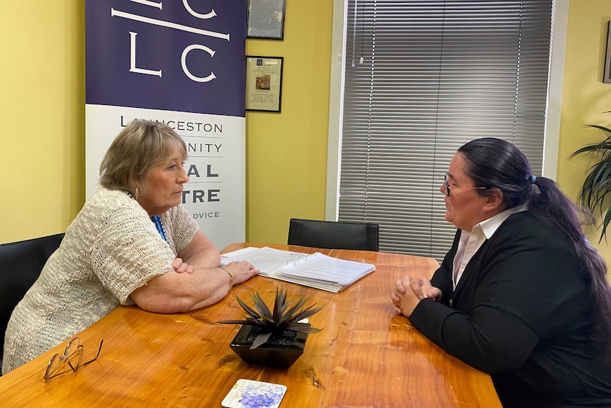 Two women sit opposite each other at a desk.