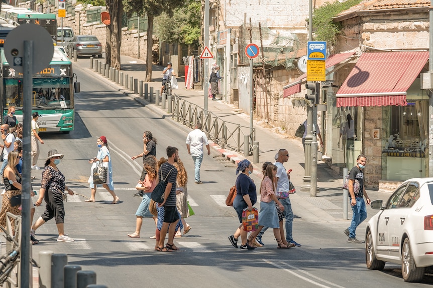 People walking across a zebra intersection in Tel Aviv as cars drive by.