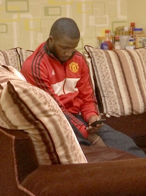 Simiyu Munyole sits on a couch looking at his phone.