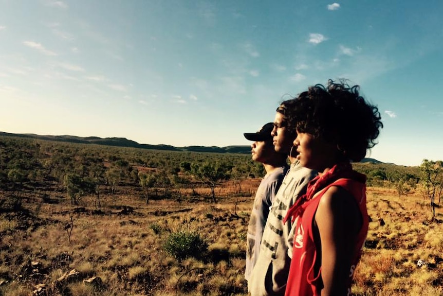Three young teenagers stand in casual clothes with the Kimberley landscape in the background.