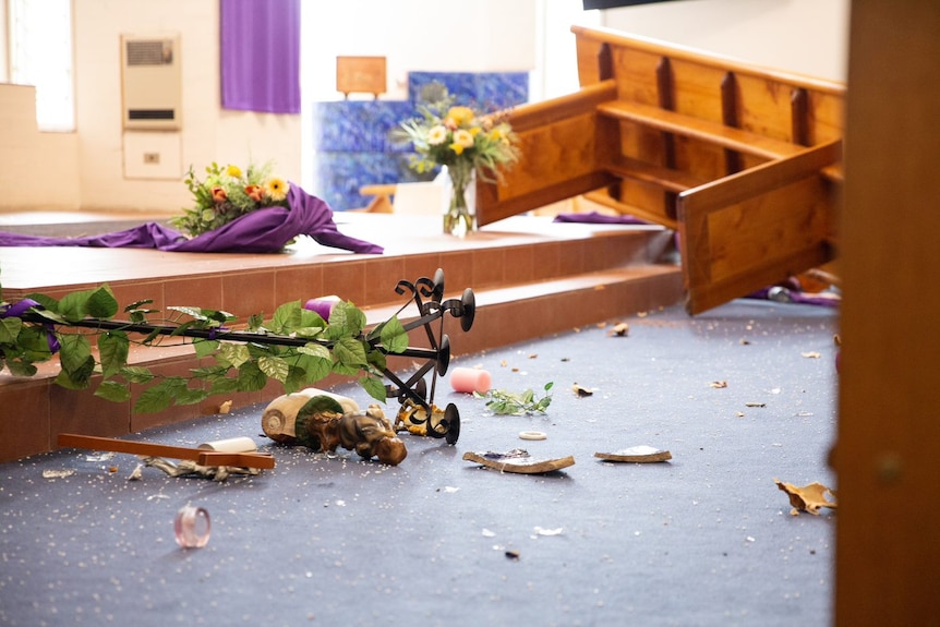 A close-up of flowers and damaged pews scattered on a church floor.