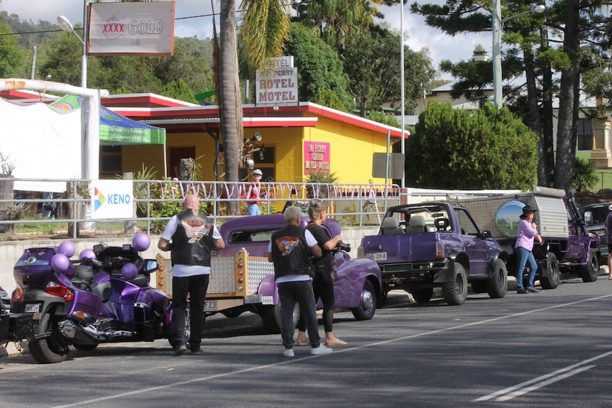 A series of purple vehicles line one side of the street in front of a bright yellow building. 