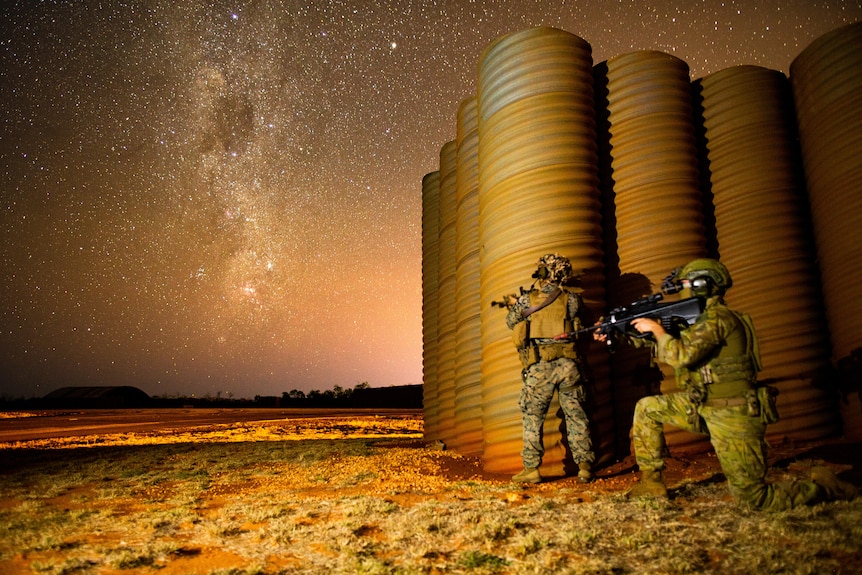 two soldiers beside tall iron tanks under the stars