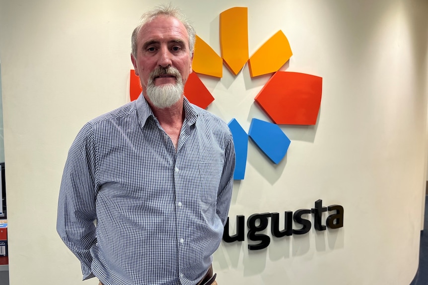 An older, bearded man standing in front of a sign that says "Port Augusta".