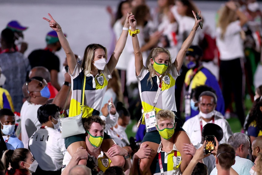 two members of team australia sit on the shoulders of two others with their arms in the air and masks on