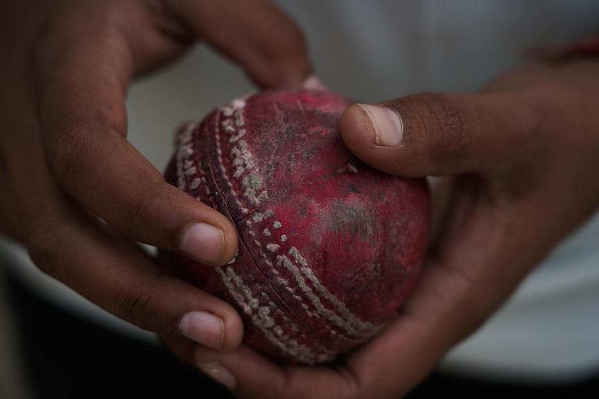A young woman holds a scuffed old cricket ball in her hands