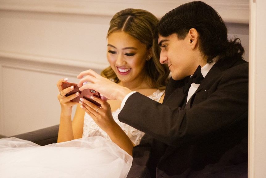A close-up photo of a young woman and a young man looking at a phone together.