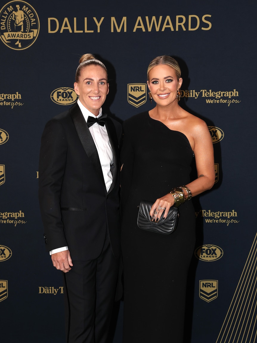 Ali Brigginshaw in a tuxedo stands with her partner in a dress on the Dally M Medal red carpet.