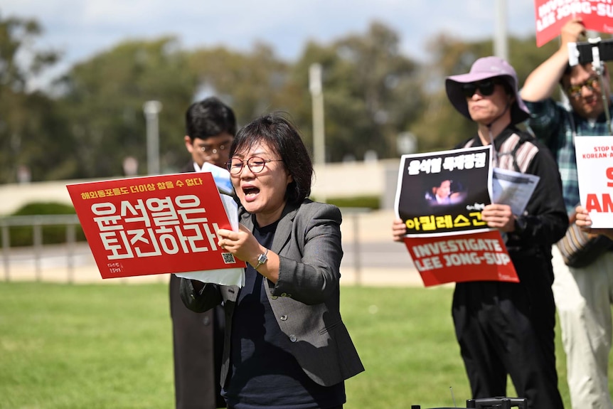 A woman wearing glasses holds up a sign while surrounded by protesters holding up signs calling to investigate Lee Jong-sup