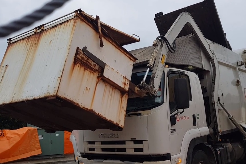 A garbage truck holding a bin suspended in the air