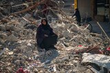 A woman in a hijab sits in rubble 
