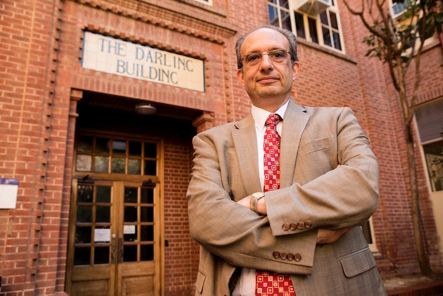 Man standing out the front of an old brick like building which is a university.