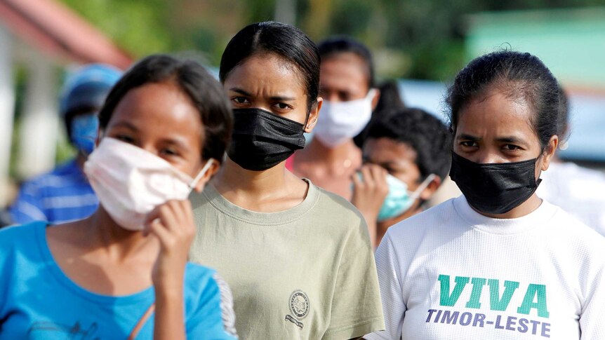 Women wearing protective masks walk down the street in Dili