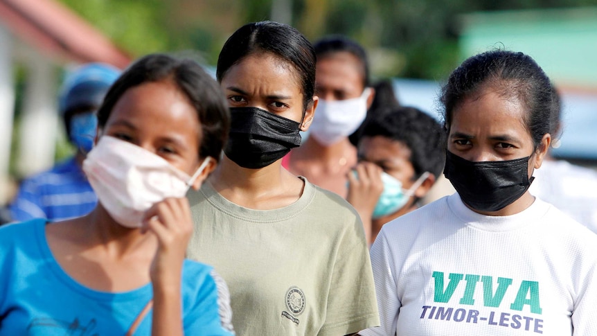 Women wearing protective masks walk down the street in Dili